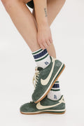 A person wearing green and blue striped retro ankle socks with a logo on the side, paired with white socks and green sneakers.