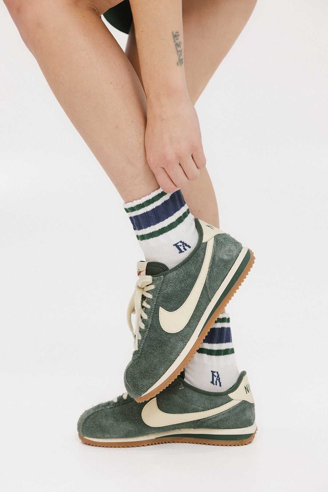 A person wearing green and blue striped retro ankle socks with a logo on the side, paired with white socks and green sneakers.