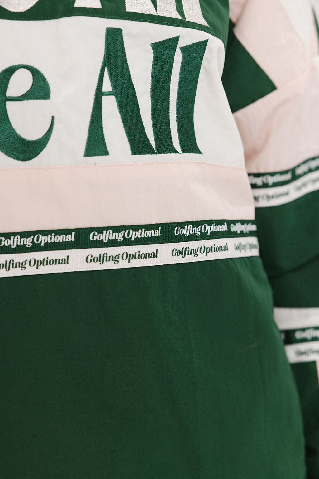 A woman wearing a green and pink racing shirt with colorblocking and text embroidery on it.