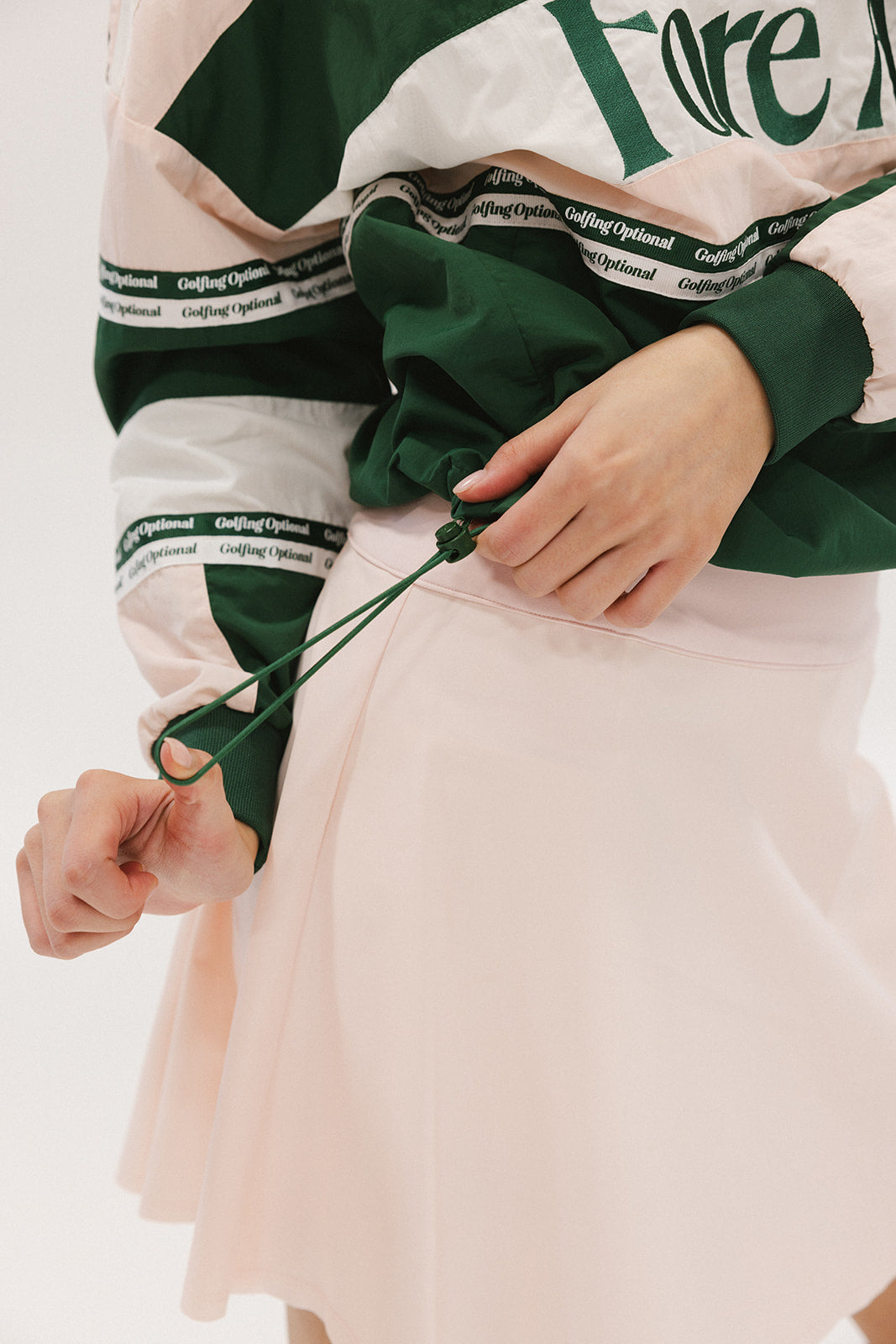A woman wearing a green and pink racing shirt with colorblocking and text embroidery on it.