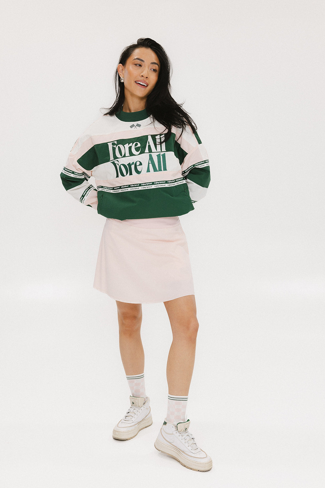A woman wearing a green and pink racing shirt with colorblocking and text embroidery on it.