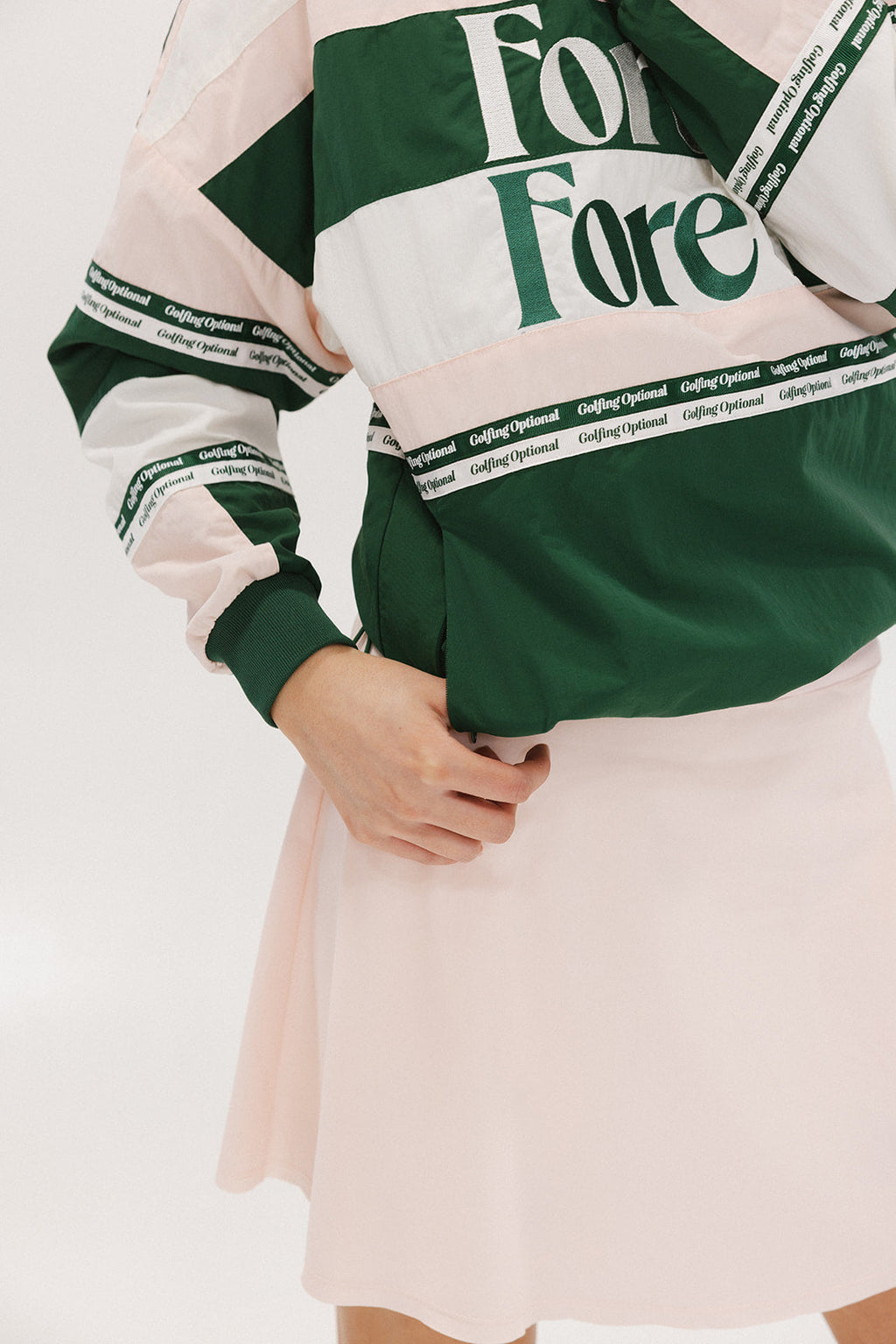 A woman wearing a green and pink racing shirt with colorblocking and text embroidery on it.