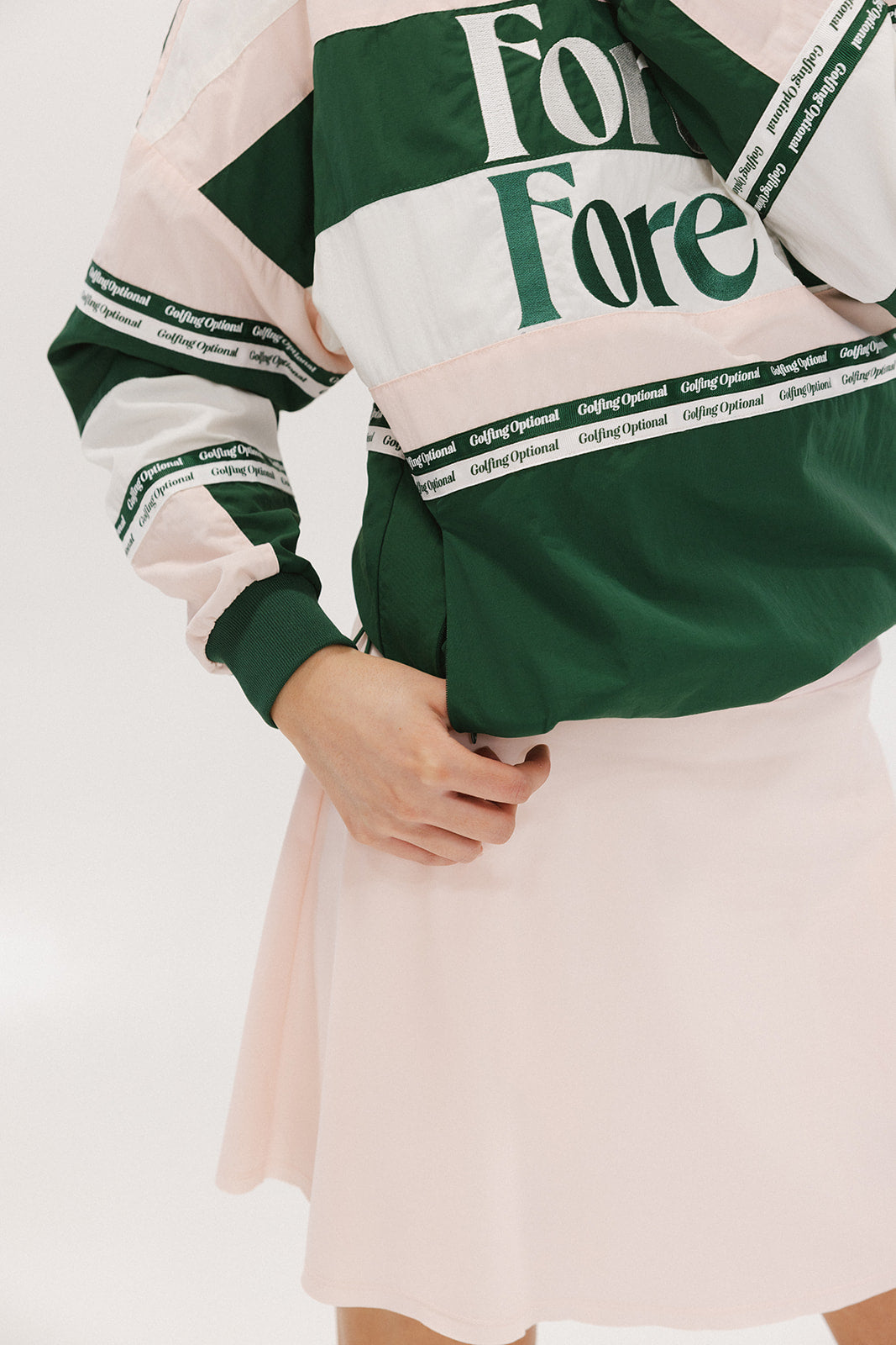 A woman wearing a green and pink racing shirt with colorblocking and text embroidery on it.