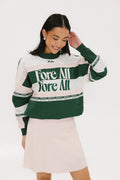 A woman wearing a green and pink racing shirt with colorblocking and text embroidery on it.