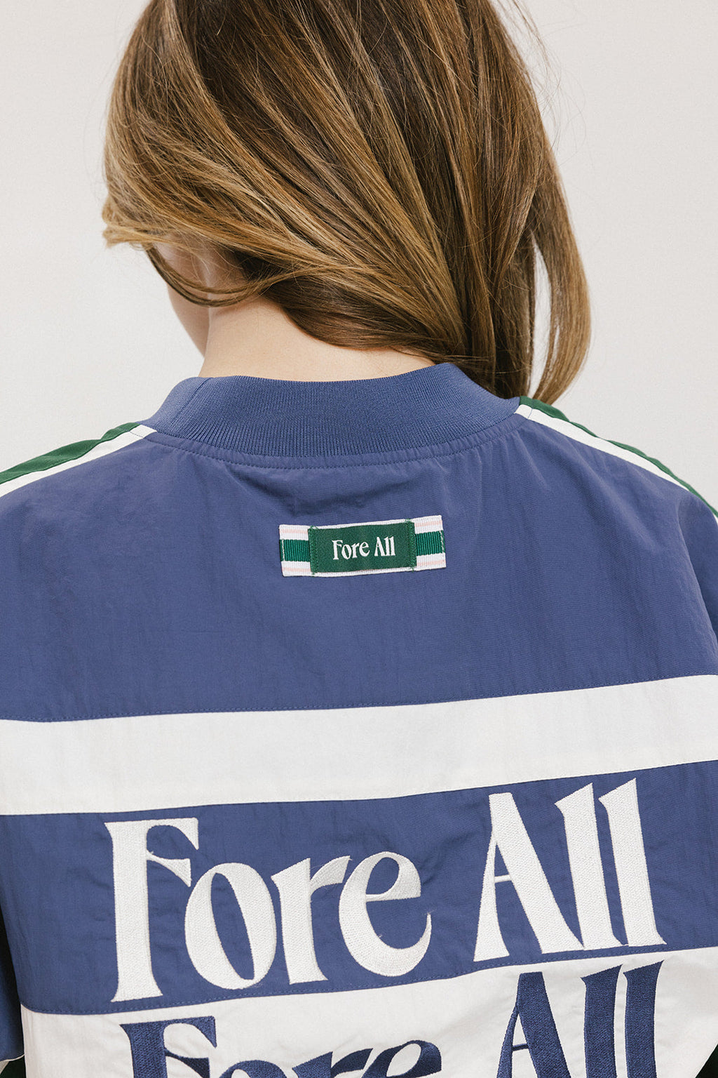 A woman wearing an indigo and green long-sleeved racing shirt with colorblocking and text embroidery.