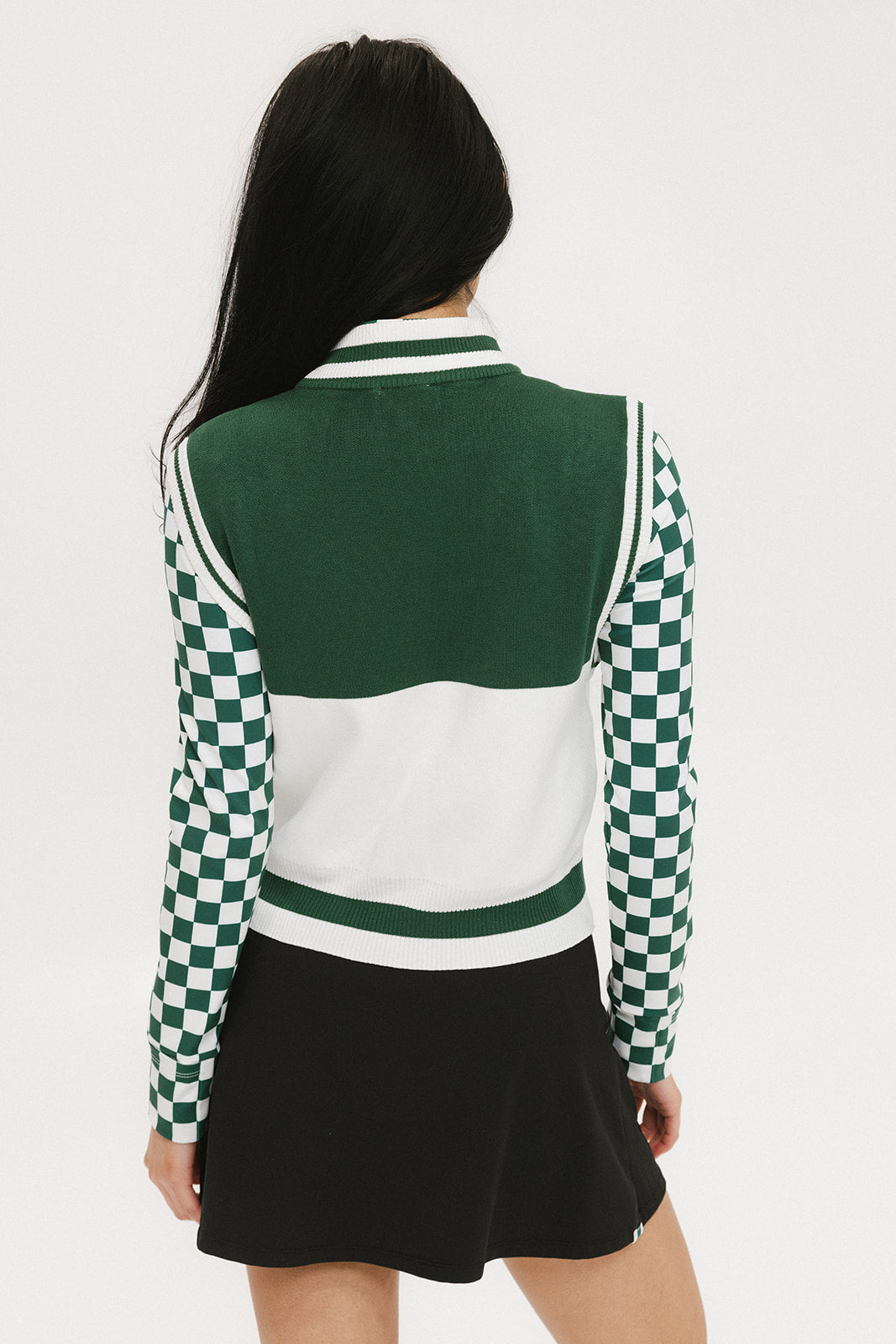 A woman wearing a sleeveless mock-neck sweater with a green and white intarsia knit design and the word 'FORE' written across the front.