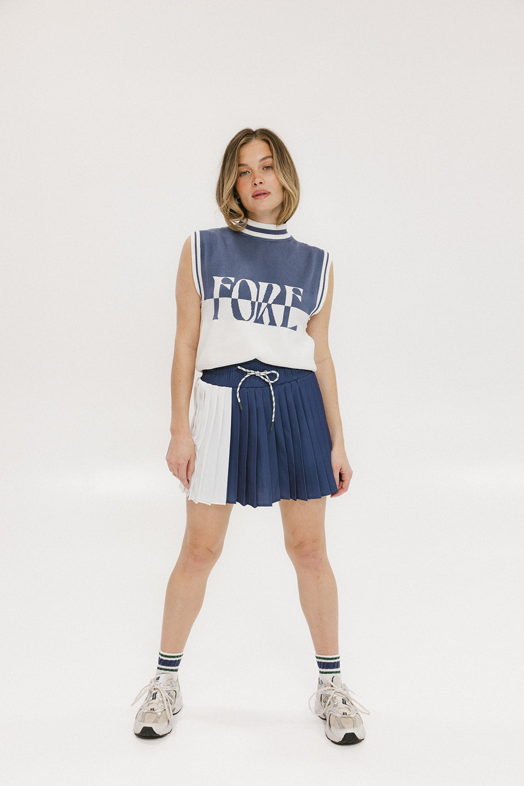 A model wearing an indigo and white intarsia mock neck, sleeveless Fore Sweater.