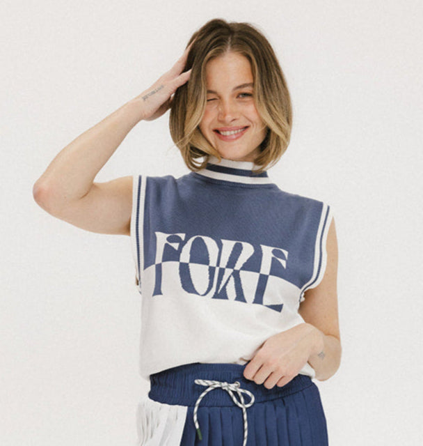 A model wearing an indigo and white intarsia mock neck, sleeveless Fore Sweater.