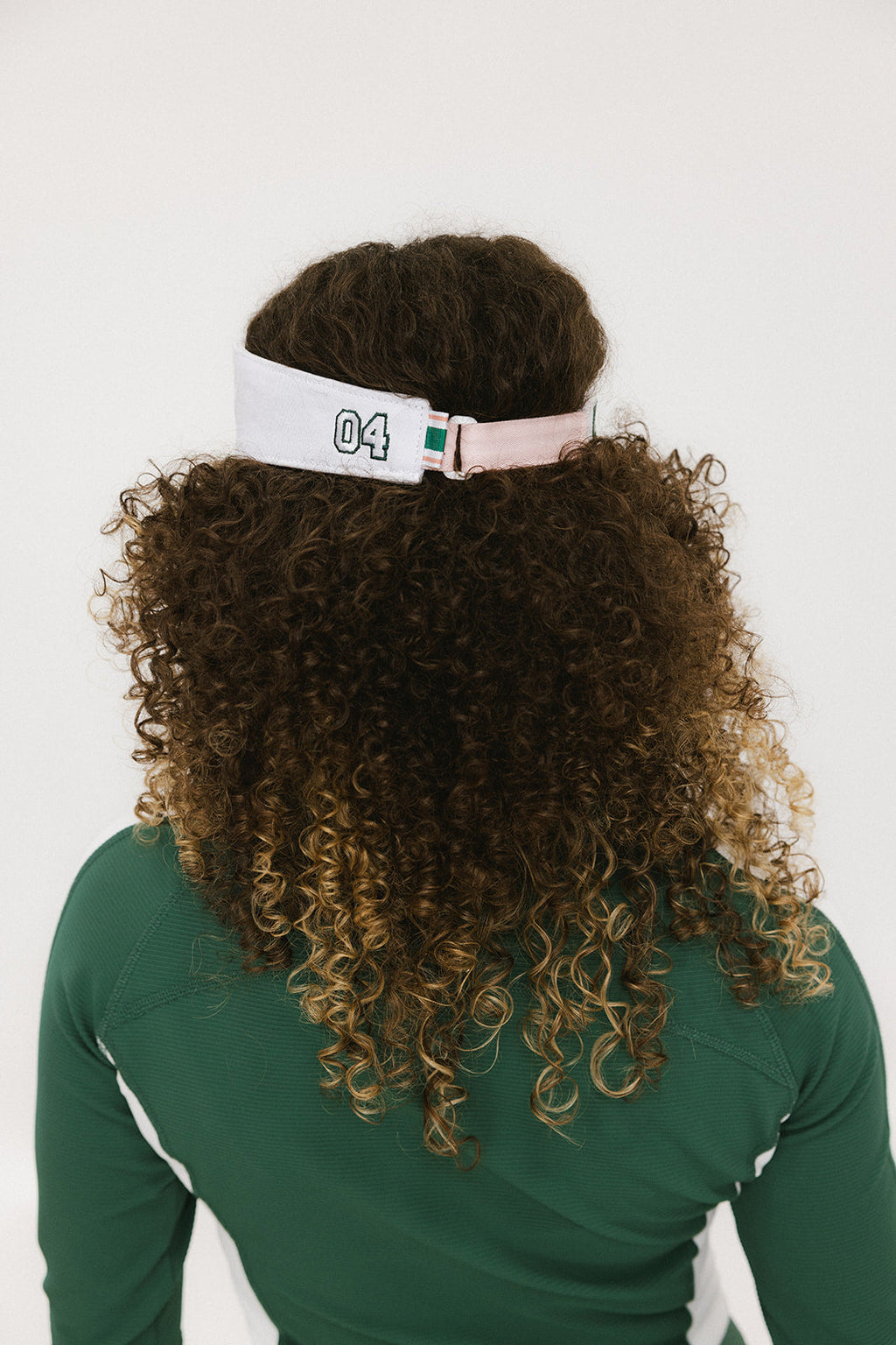 A woman wearing a pink and white 'FORE' visor and a green long-sleeved shirt.