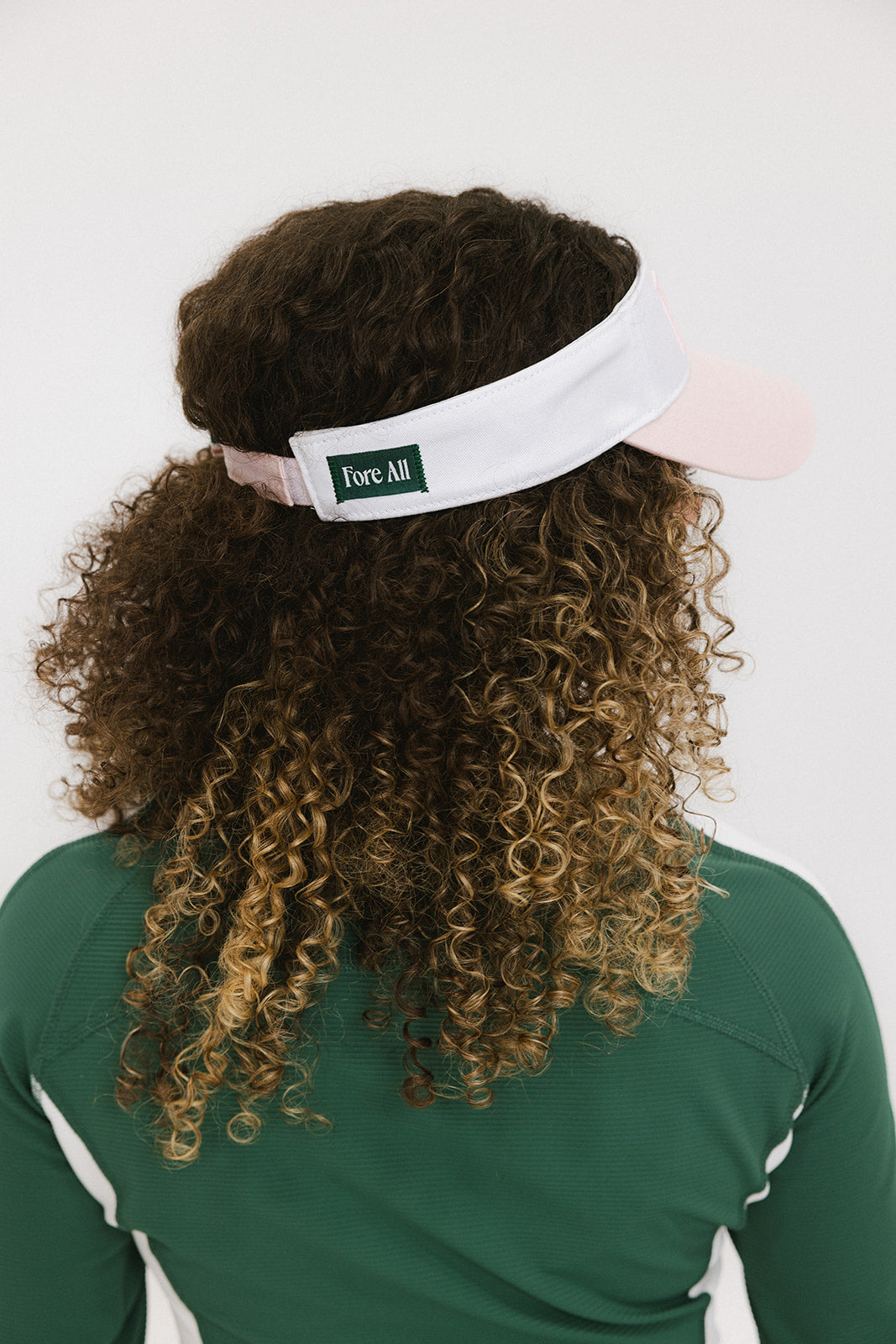 A woman wearing a pink and white 'FORE' visor and a green long-sleeved shirt.
