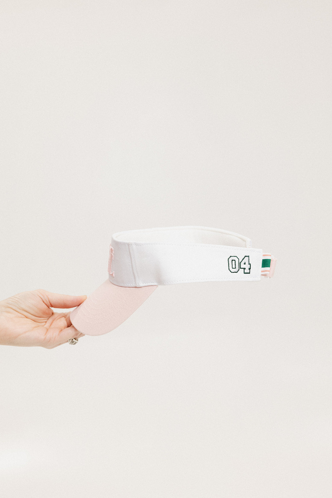 A hand holding a two-toned visor with 'FORE' logo in pink and white colors.