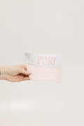 A hand holding a two-toned visor with 'FORE' logo in pink and white colors.