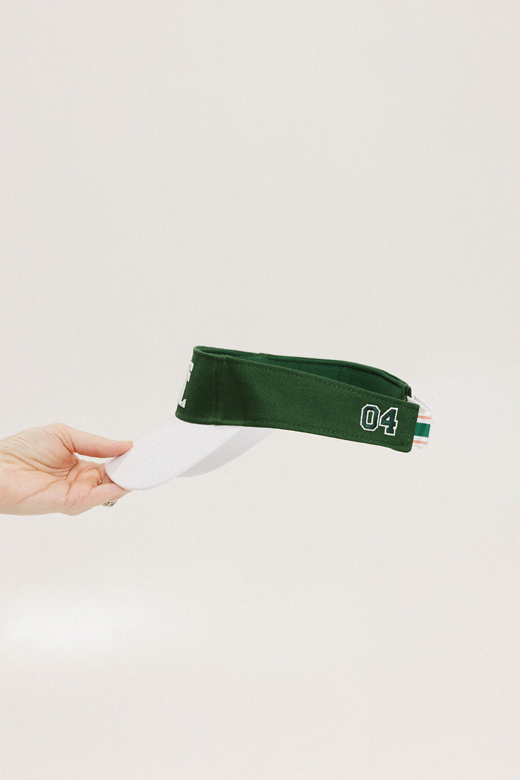 A hand holding a white and green two-toned visor with the word '04' printed on the back.