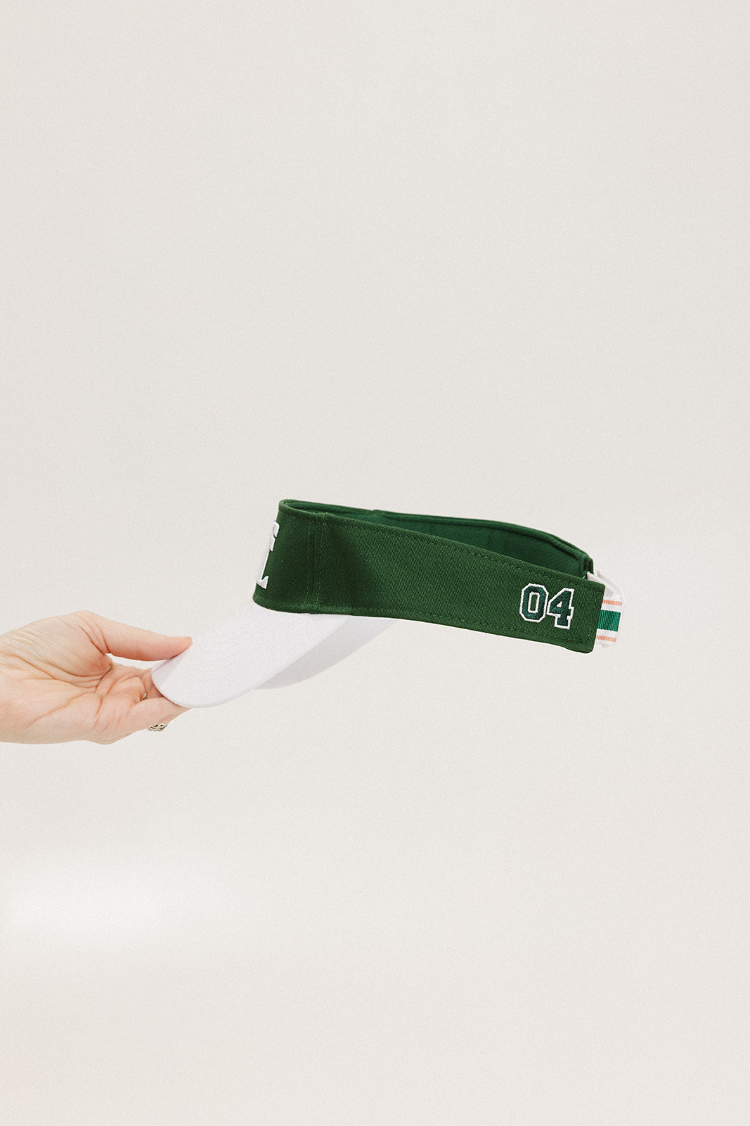 A hand holding a white and green two-toned visor with the word '04' printed on the back.