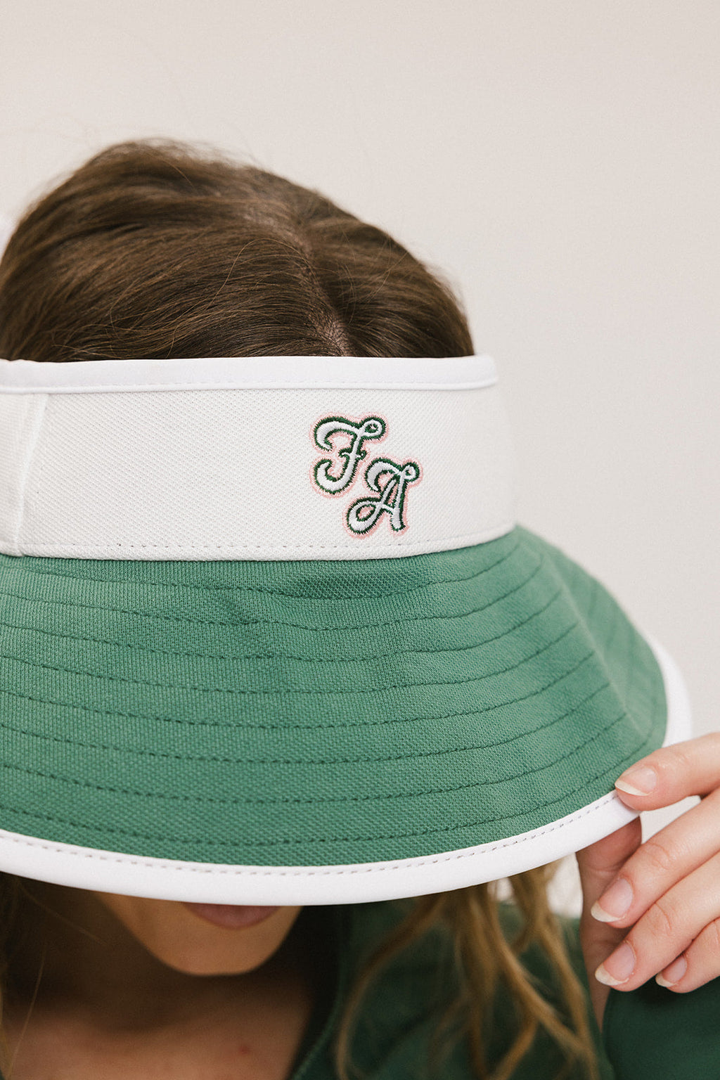 A woman wearing a white and green visor with a 'FA' logo on the front.