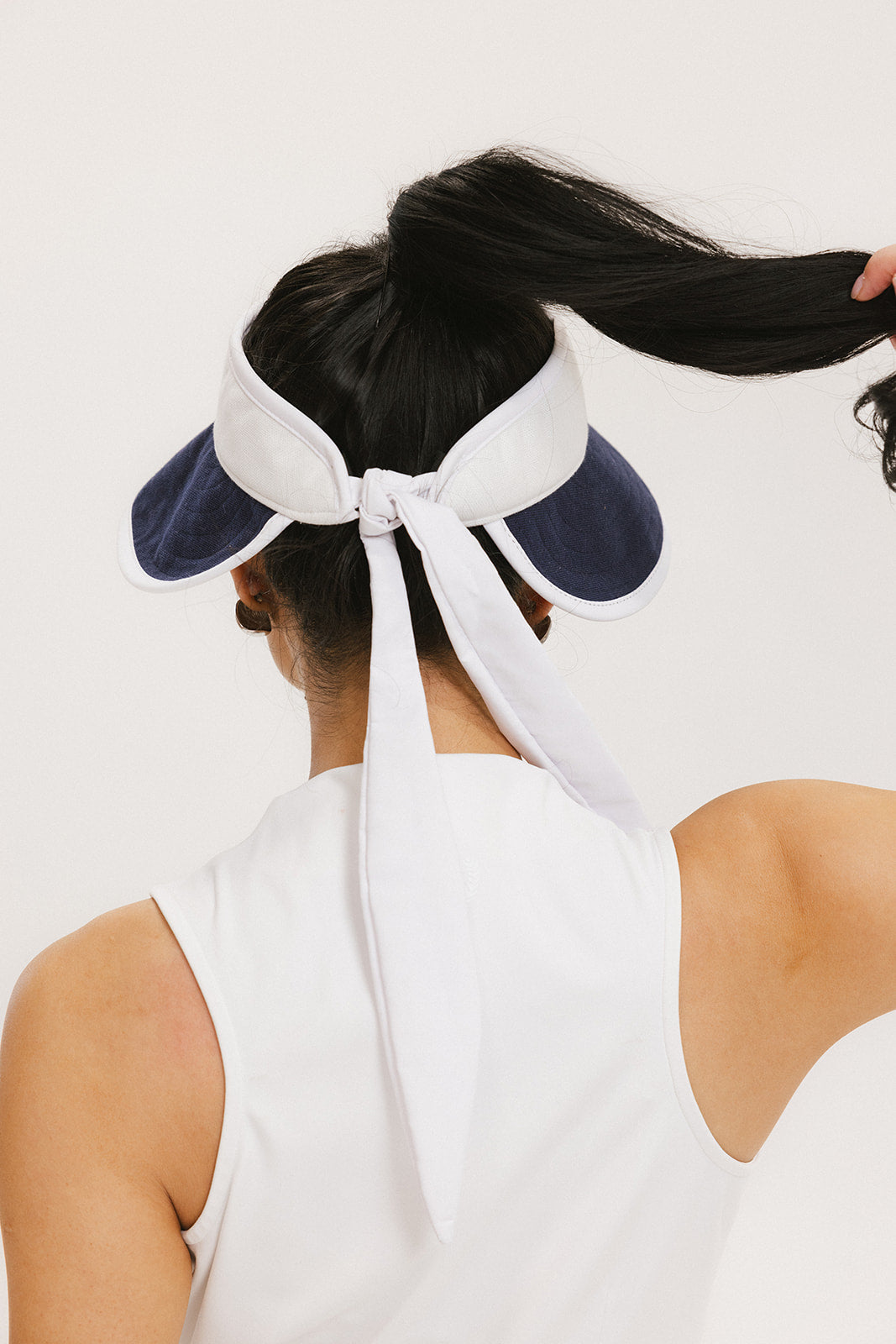 A woman wearing a white and indigo visor with a 'FA' logo on the front and a tied bow on the back.