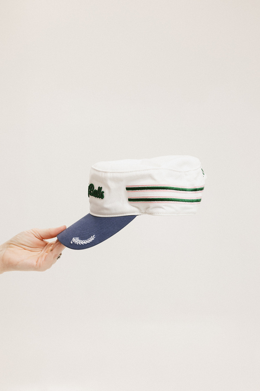 A hand holding a white and blue structured cap with 'Chasing Balls' text and stripes.