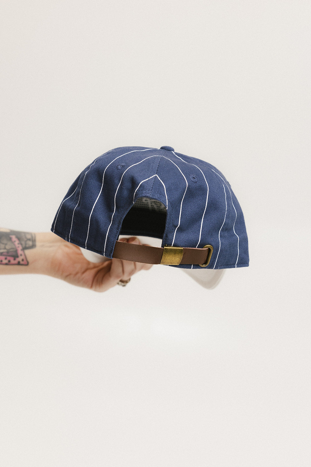 A hand holding a blue and white striped baseball cap with an embroidered logo