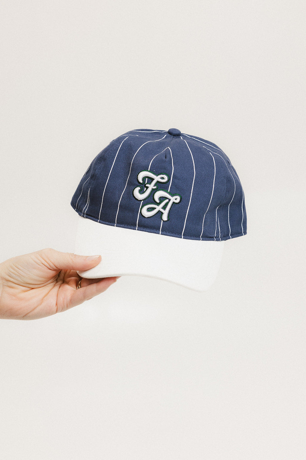 A hand holding a blue and white striped baseball cap with an embroidered logo
