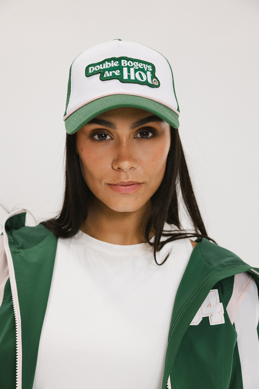 A model wearing a trucker hat with 'Double Bogeys Are Hot' text embroidered on the front, featuring a white mesh back and green visor.