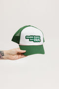 A hand holding a trucker hat with 'Double Bogeys Are Hot' text embroidered on the front, featuring a white mesh back and green visor.