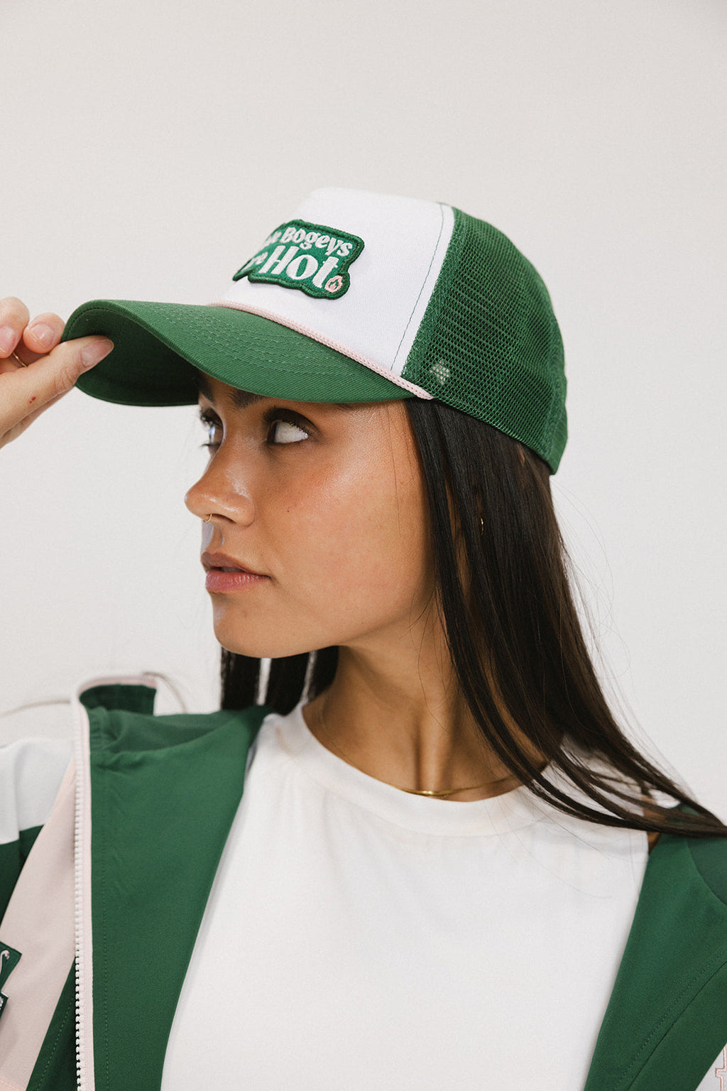 A model wearing a trucker hat with 'Double Bogeys Are Hot' text embroidered on the front, featuring a white mesh back and green visor.
