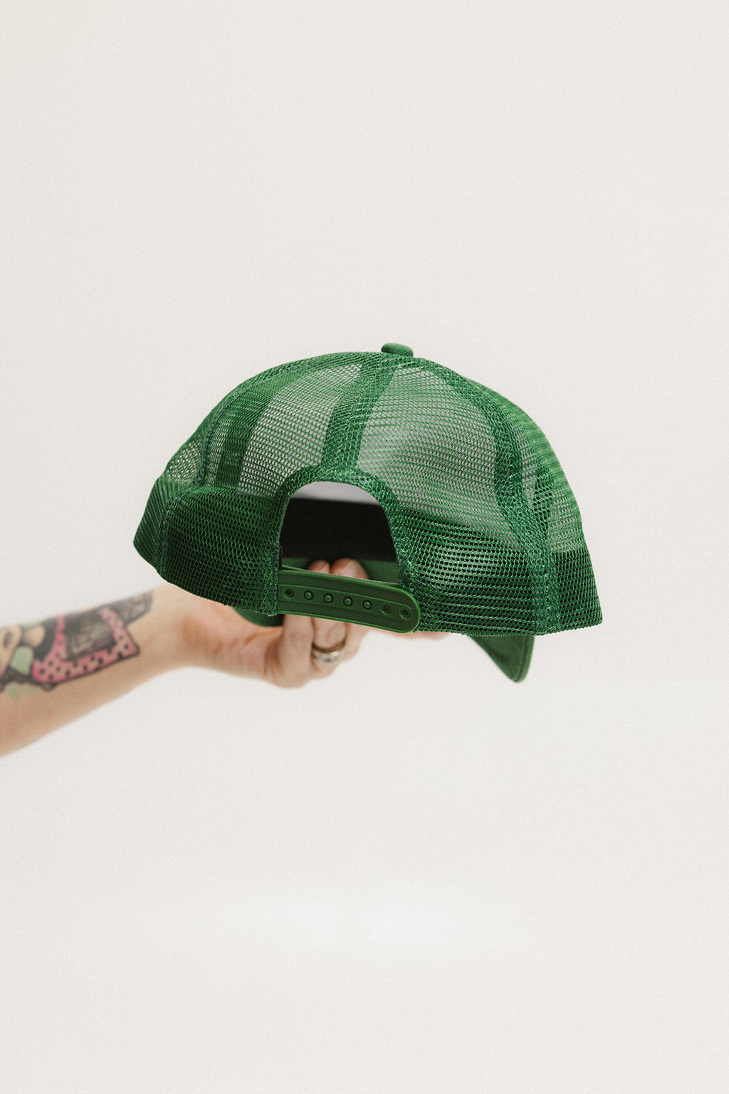 A hand holding a white and green trucker hat with the brim facing up.