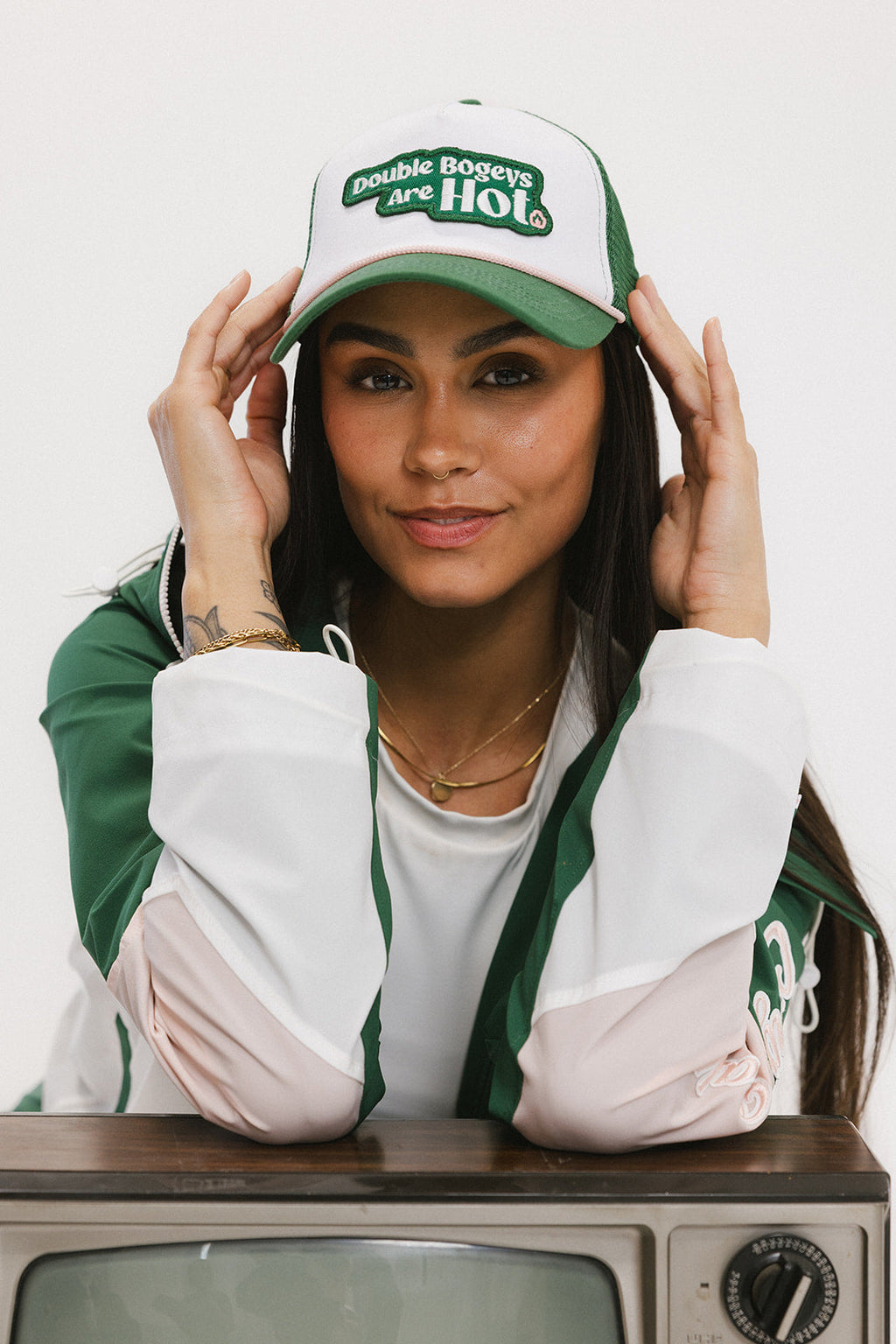 A model wearing a trucker hat with 'Double Bogeys Are Hot' text embroidered on the front, featuring a white mesh back and green visor.