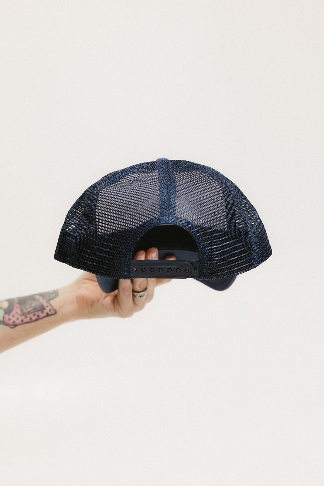 A hand holding a trucker hat with a white front and indigo blue mesh back.