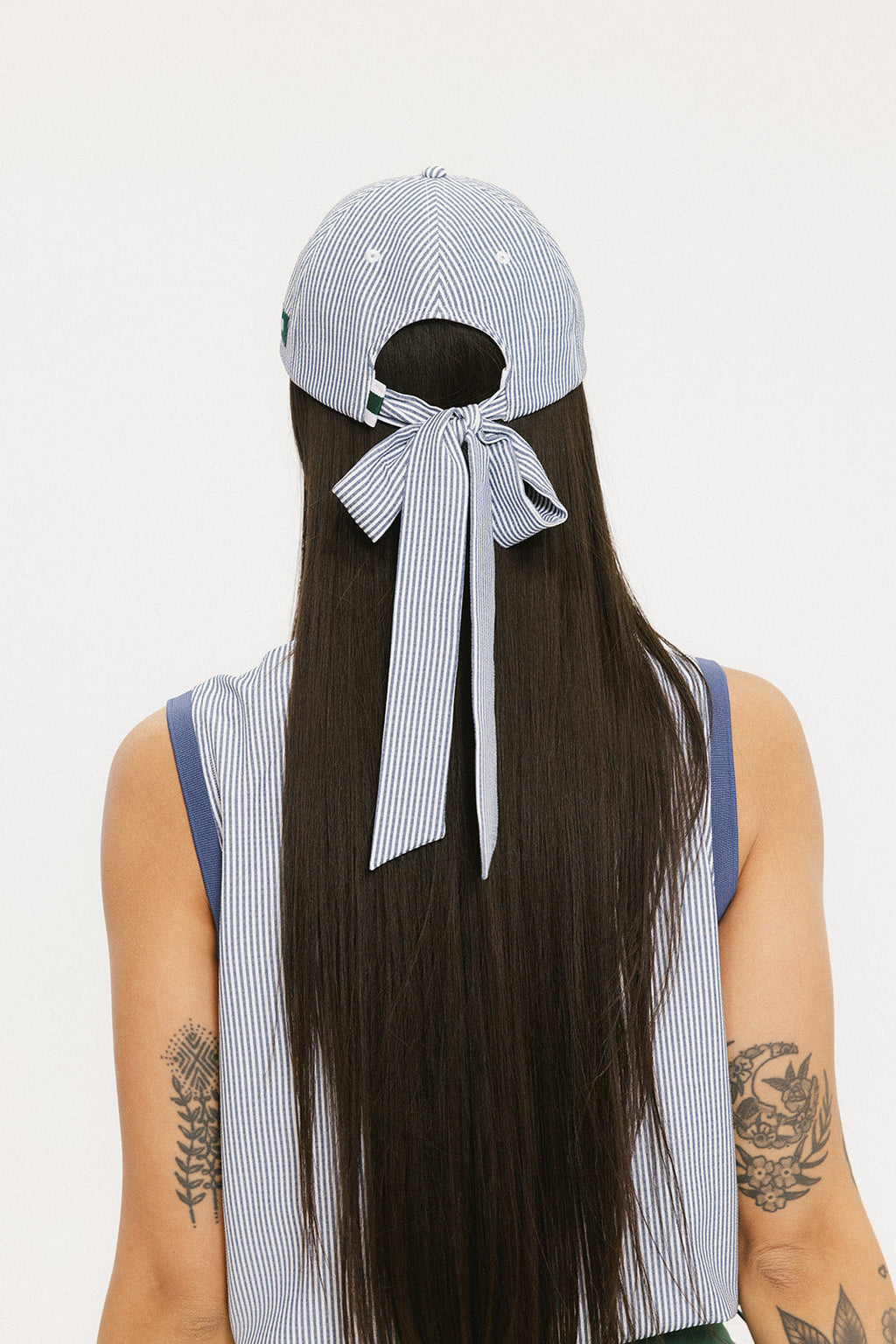 A person wearing a blue and white seersucker baseball cap with the text 'Chasing Balls' embroidered on the front and an oversized bow at the back.