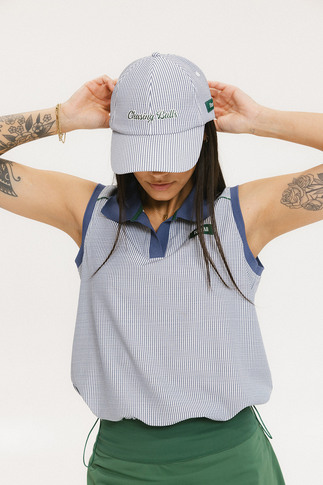 A person wearing a blue and white seersucker baseball cap with the text 'Chasing Balls' embroidered on the front and an oversized bow at the back.