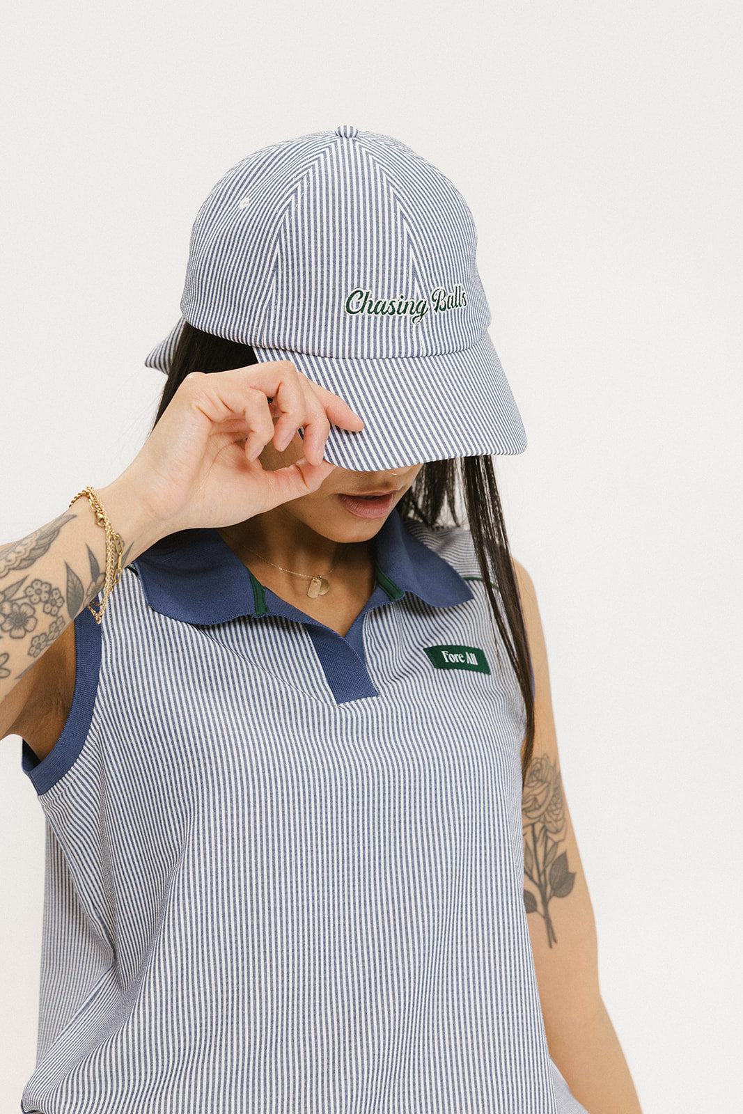 A person wearing a blue and white seersucker baseball cap with the text 'Chasing Balls' embroidered on the front and an oversized bow at the back.