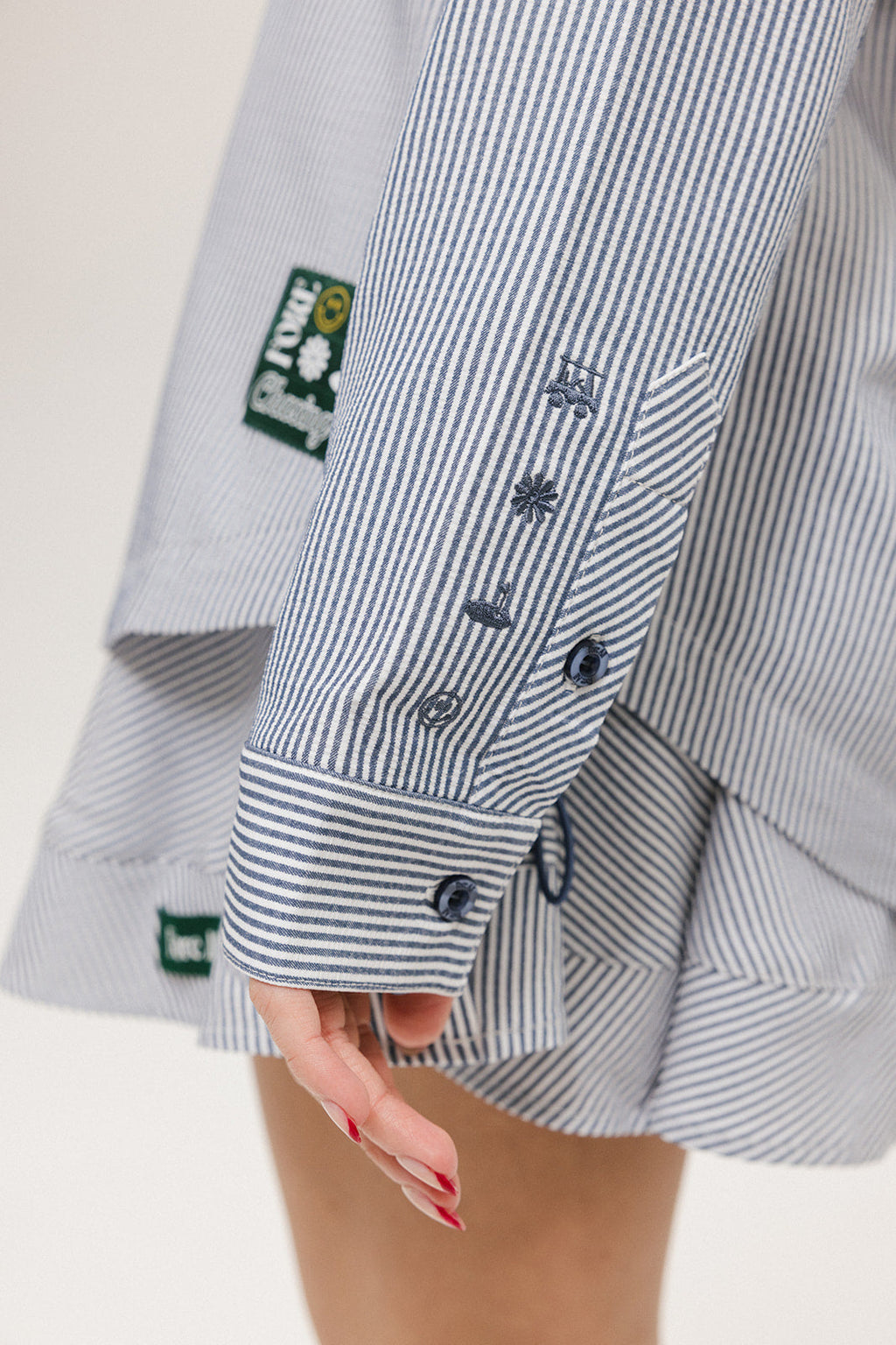 A woman wearing a long, button-up shirt with indigo stripes, featuring a collar, button-down front, and elastic toggles at the side seam hem and sleeve cuffs