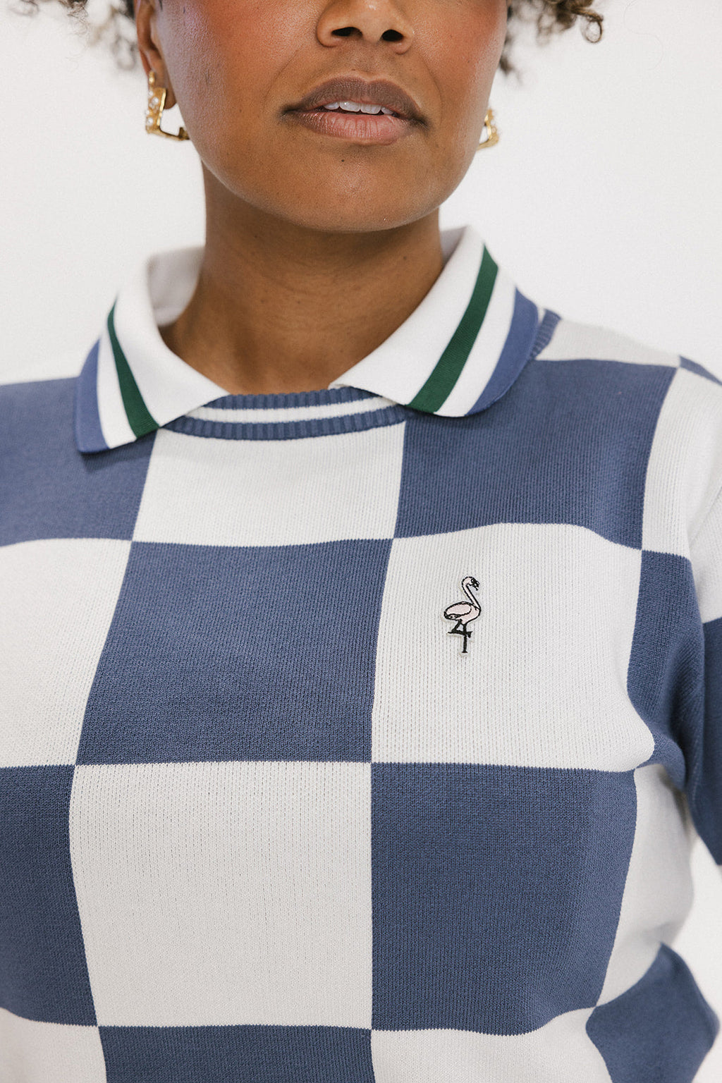 A woman wearing a sleeveless, checkered indigo and white sweater with a mock neck.