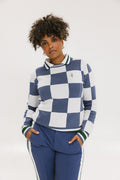 A woman wearing a sleeveless, checkered indigo and white sweater with a mock neck.