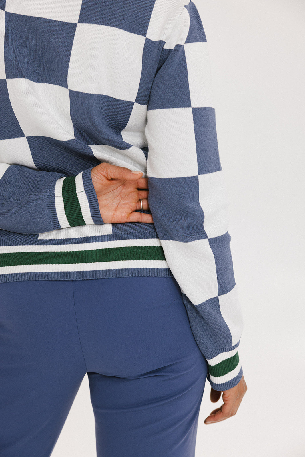 A person wearing a checkered blue and white sweater with green accents and solid blue pants.