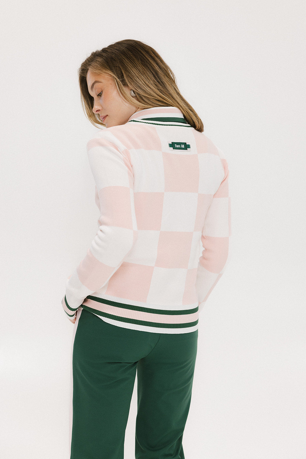 A person is shown from the back wearing a pink and white checkered sweater with a green stripe, paired with green pants.