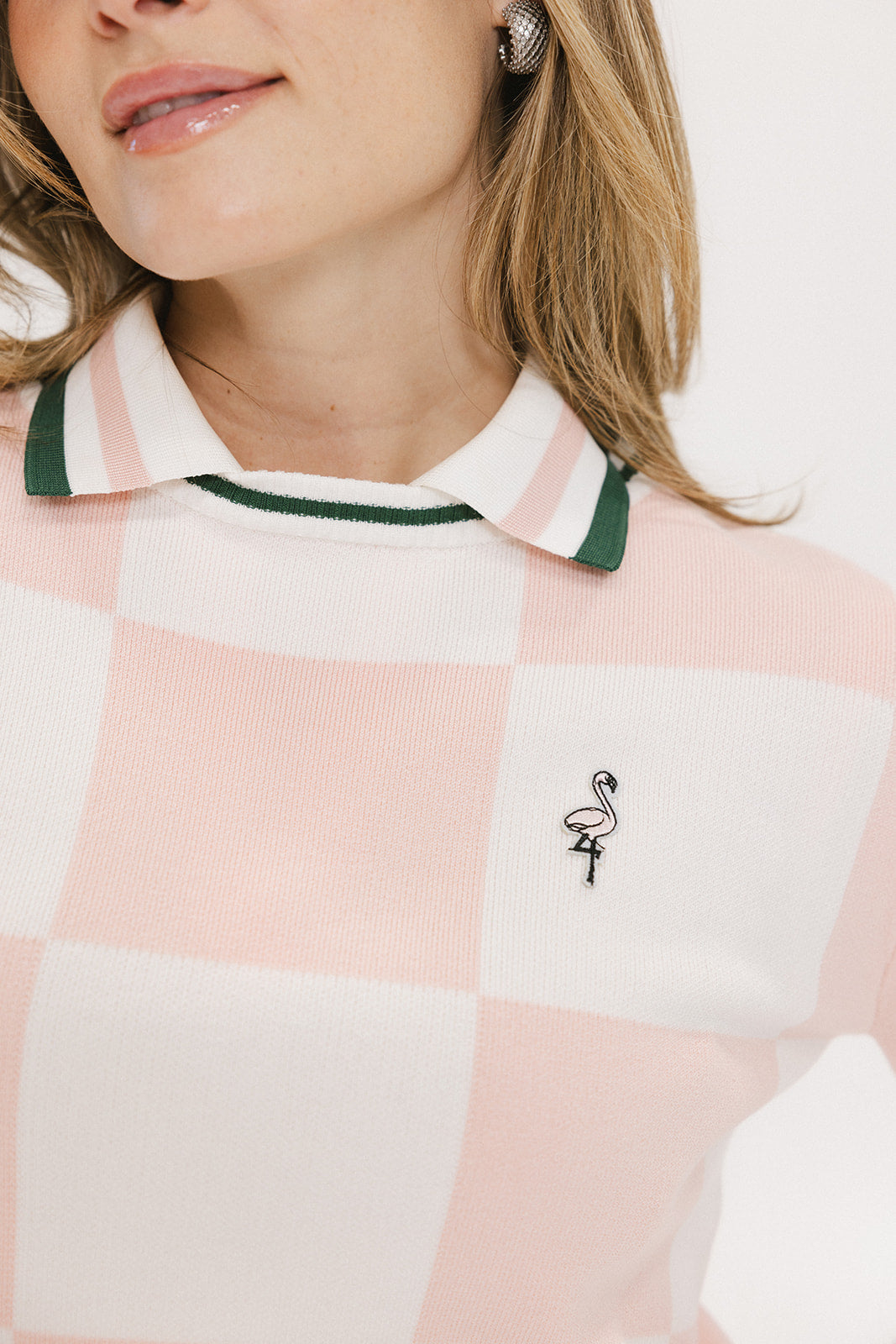 A woman wearing a pink and white checkered intarsia knit sleeveless sweater with a rounded neck.