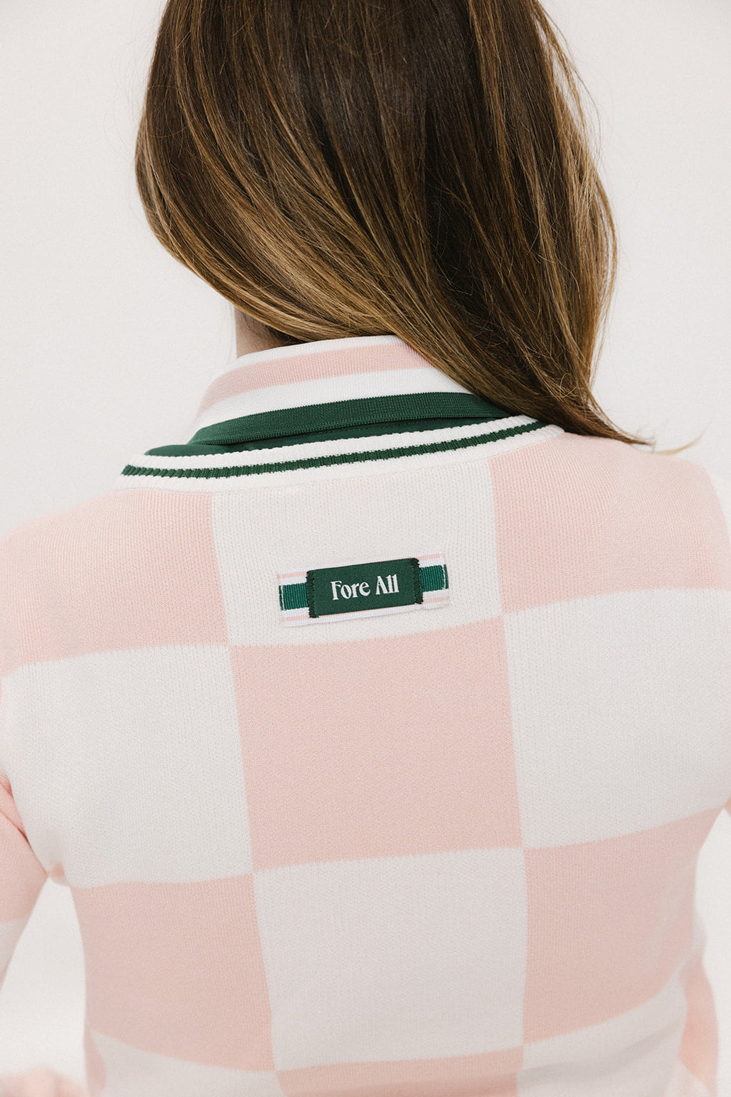A woman wearing a pink and white checkered intarsia knit sleeveless sweater with a rounded neck.