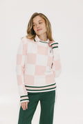 A woman wearing a pink and white checkered intarsia knit sleeveless sweater with a mock neck.