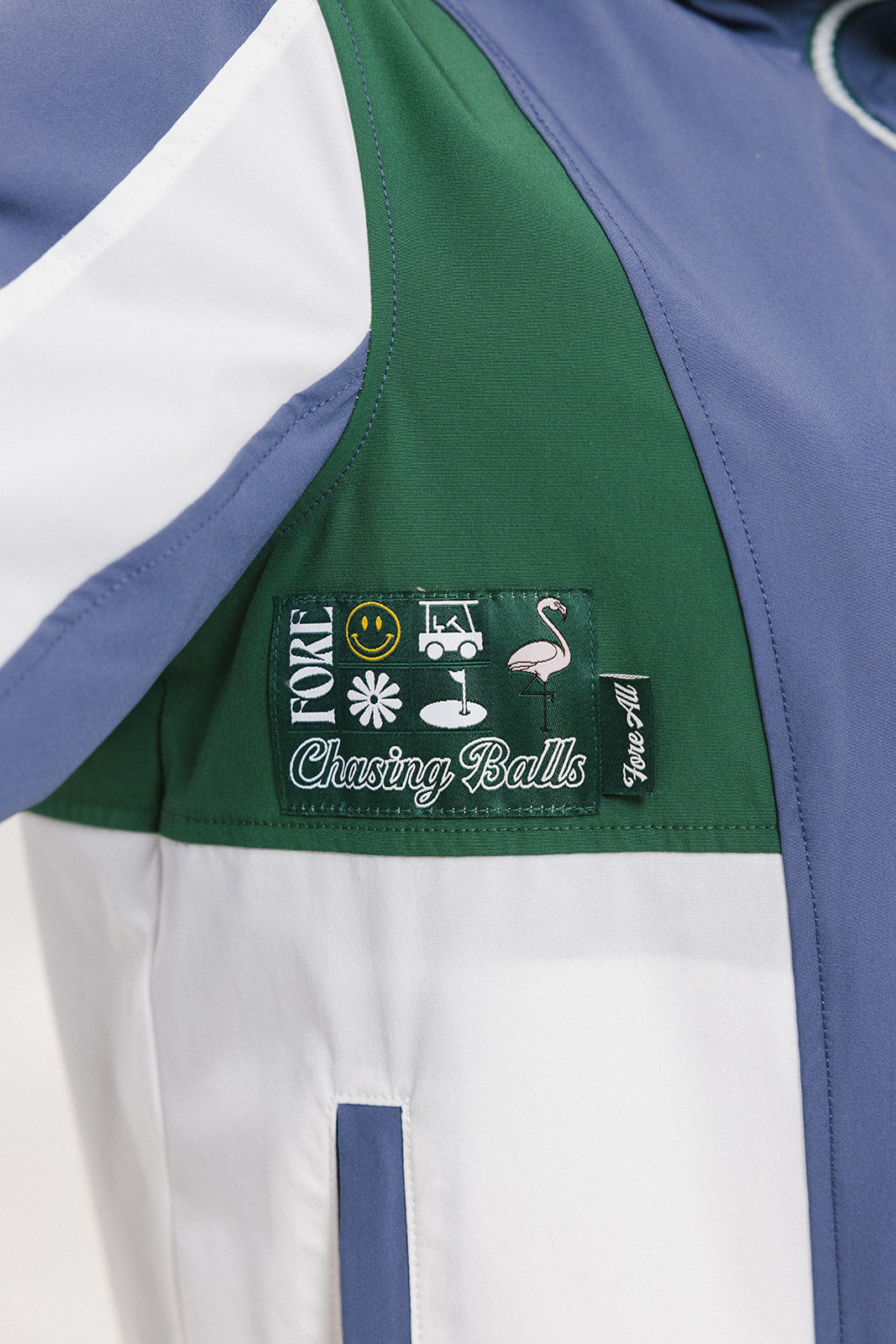 A detail view of a Caitlin Warm-Up Jacket showing a color block design with green, blue, and white panels, and a logo patch on the sleeve.