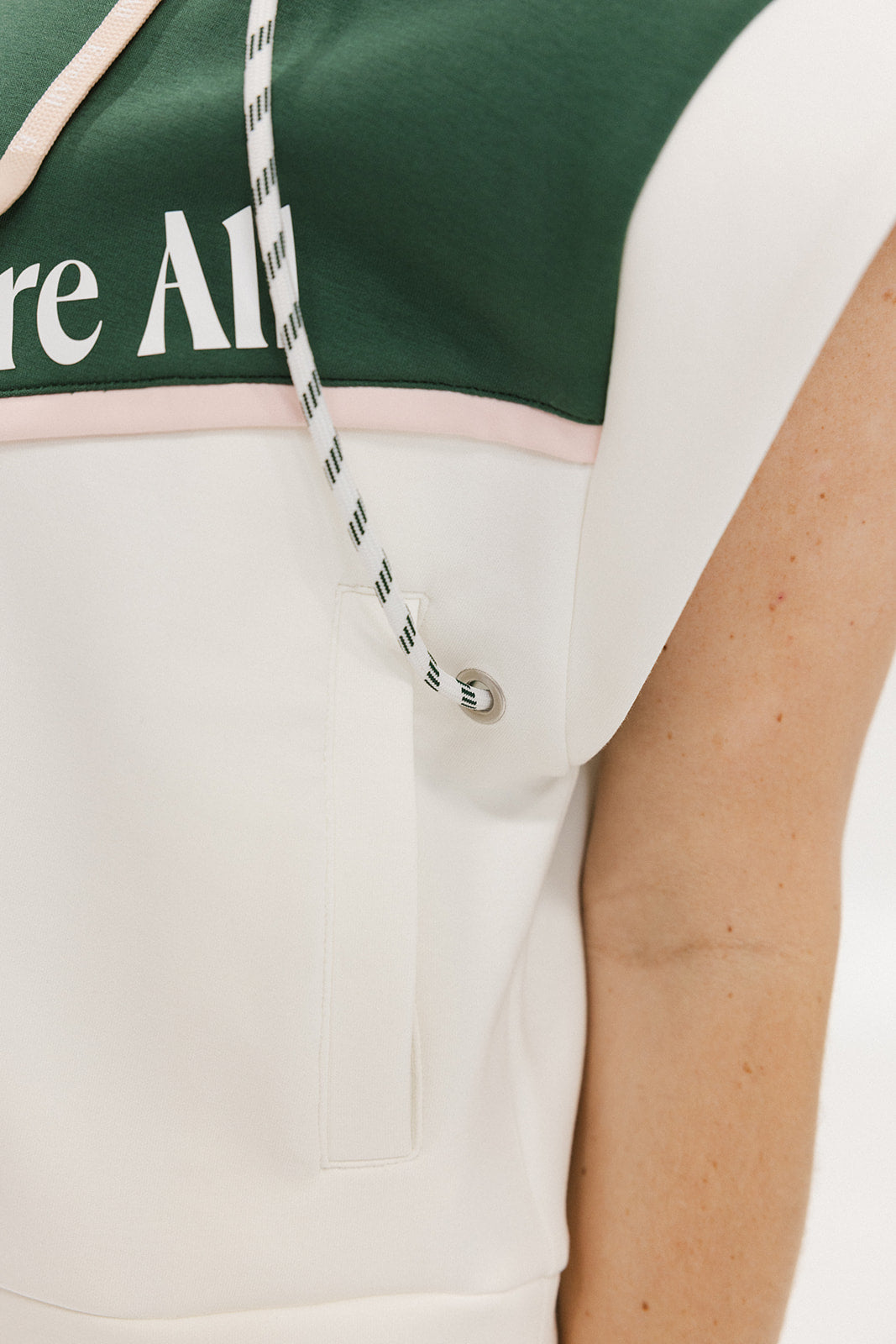 A person wearing a green and white sleeveless hoodie with a hood, matching green and white checkered hat, and green and white checkered skirt. The hoodie has white text and branding on it.