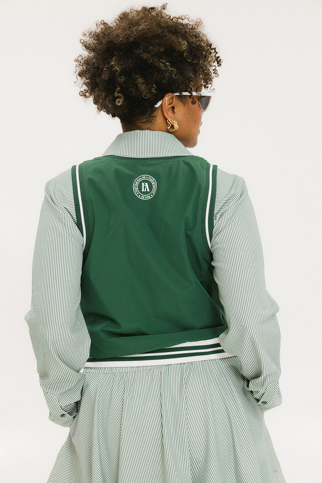 A woman wearing a green sleeveless windbreaker vest with a collar, featuring a white appliquéd logo on the left chest and silicone logos on the upper back.