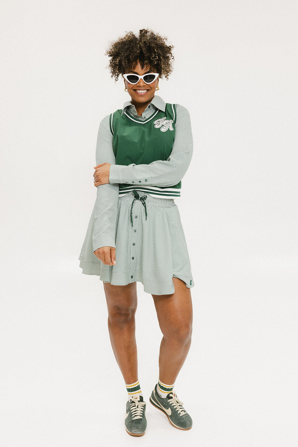 A woman wearing a green sleeveless windbreaker vest with a collar, featuring a white appliquéd logo on the left chest and silicone logos on the upper back.