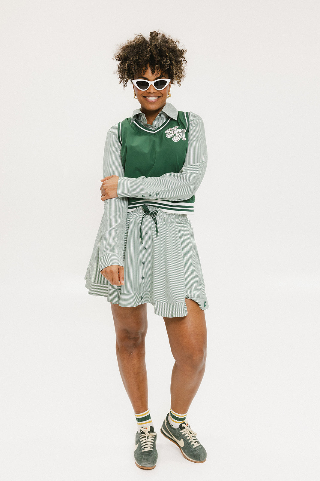 A woman wearing a green sleeveless windbreaker vest with a collar, featuring a white appliquéd logo on the left chest and silicone logos on the upper back.