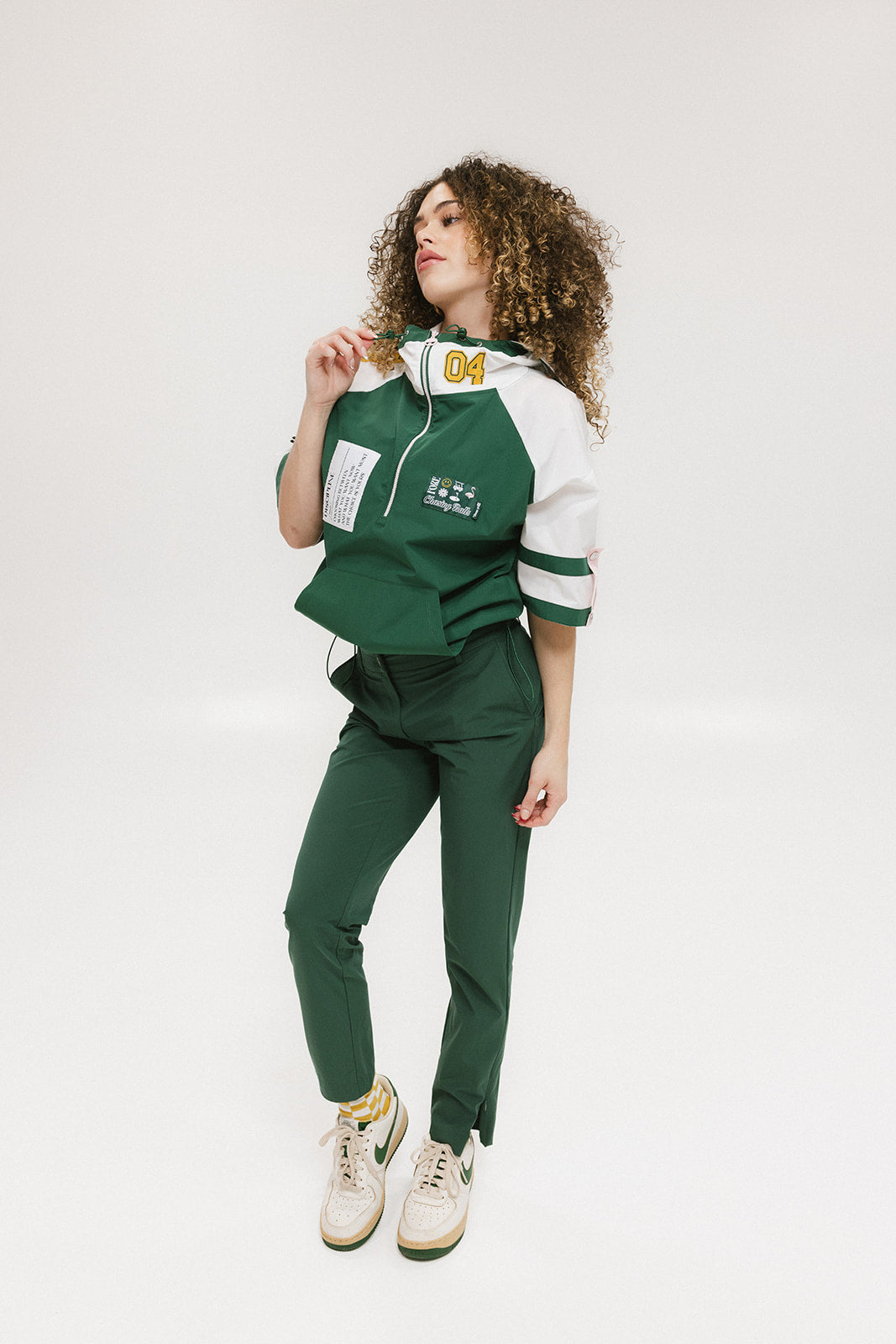A woman wearing a green and white hoodie with a half-zip design, kangaroo pocket, and decorative woven ribbons.
