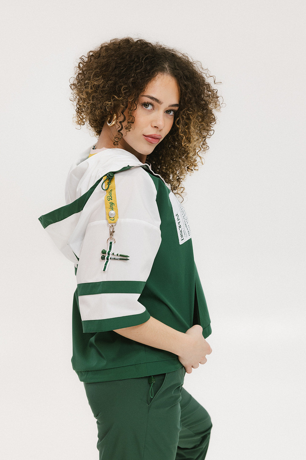A woman wearing a green and white hoodie with a half-zip design, kangaroo pocket, and decorative woven ribbons.