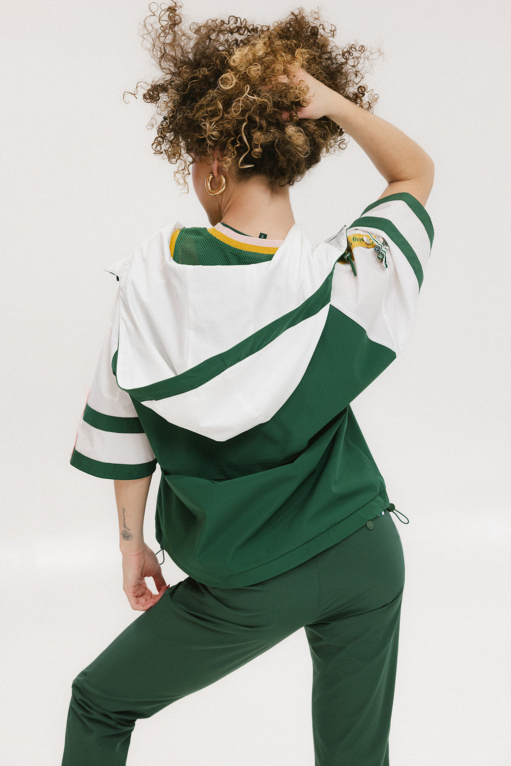 A woman wearing a green and white hoodie with a half-zip design, kangaroo pocket, and decorative woven ribbons.