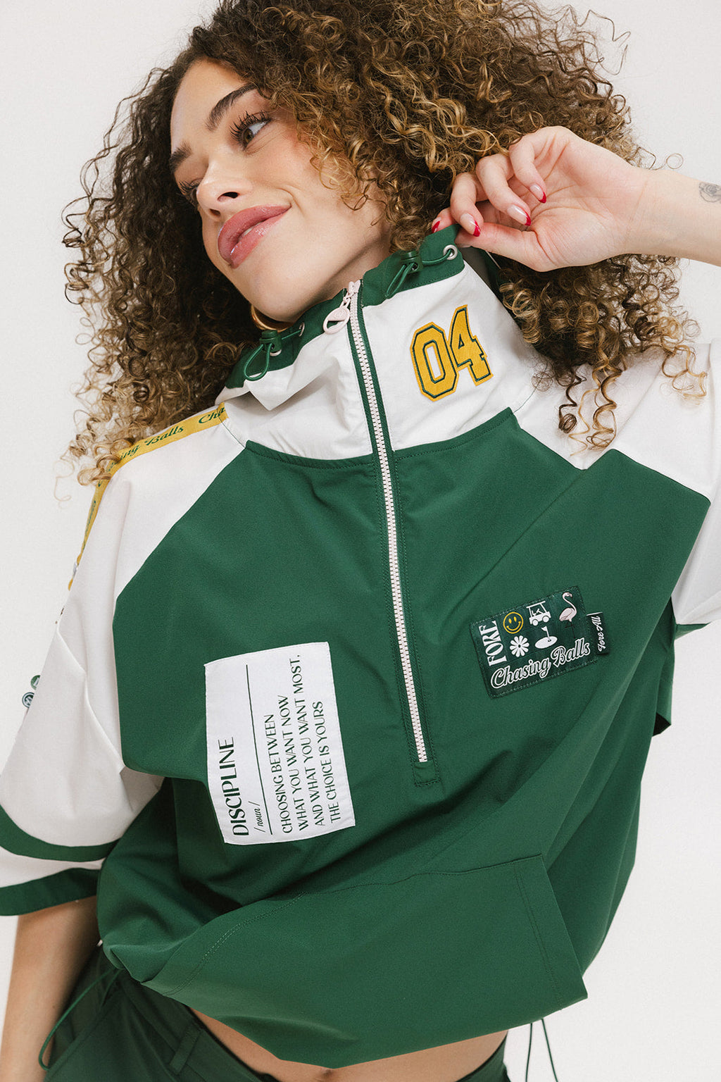 A woman wearing a green and white hoodie with a half-zip design, kangaroo pocket, and decorative woven ribbons.