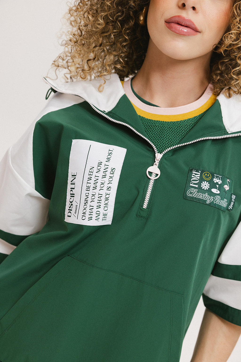 A woman wearing a green and white hoodie with a half-zip design, kangaroo pocket, and decorative woven ribbons.